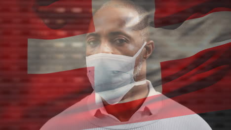 animation of flag of switzerland waving over man wearing face mask during covid 19 pandemic