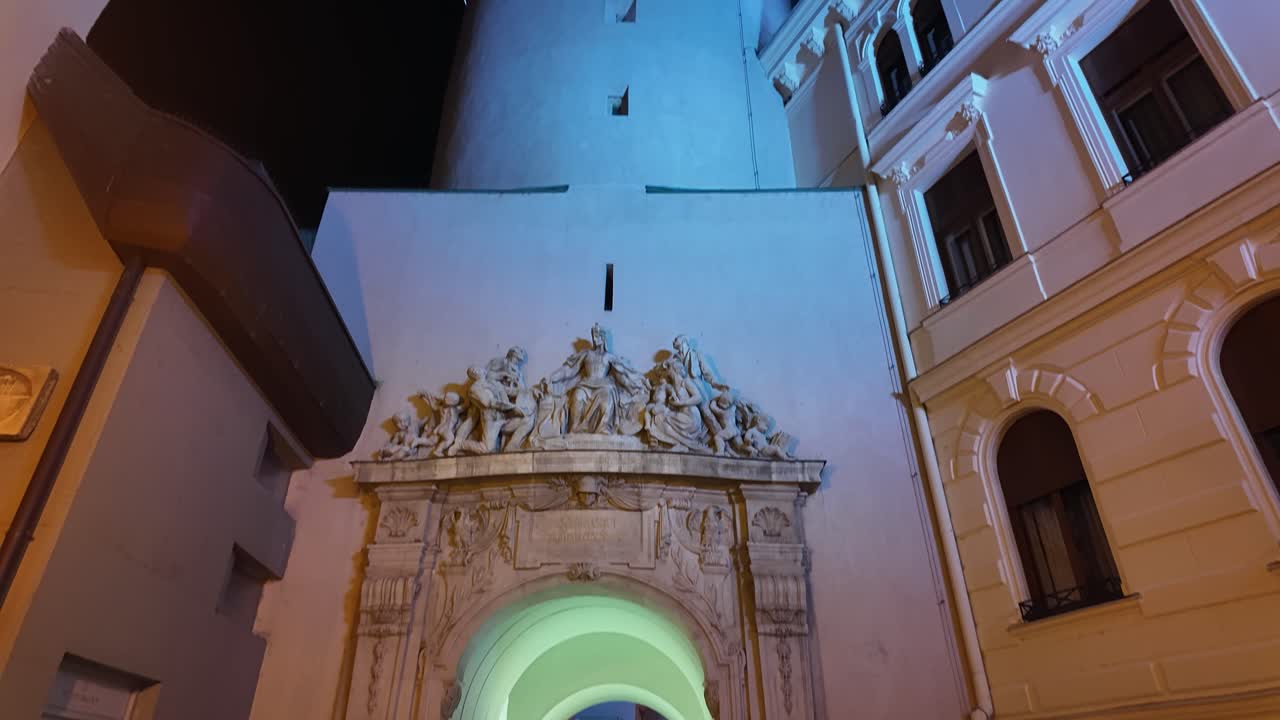 Camera tilt-up showing the Fire Tower in downtown Sopron at night, with illuminated architecture and surrounding buildings.