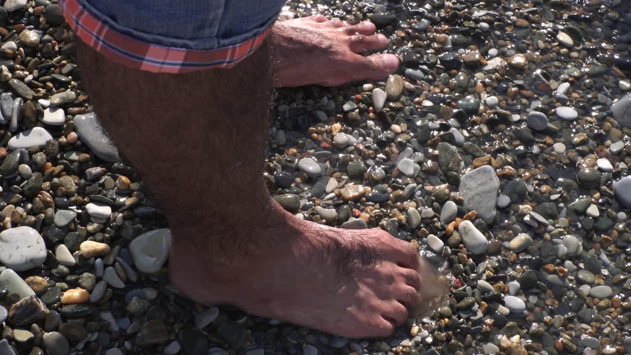 los pies de una persona en el agua en una playa de guijarros
