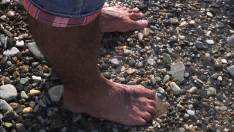 person's feet in the water on a pebble beach