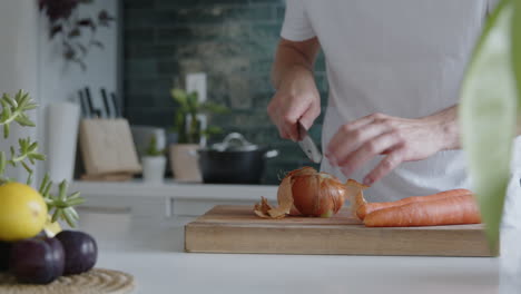 Plano-Medio-De-Un-Hombre-Pelando-Una-Cebolla-Fresca-Con-Las-Manos-En-Una-Cocina-Moderna