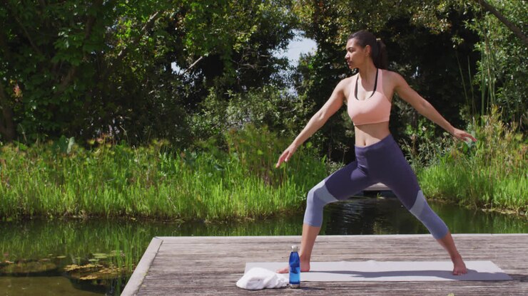 Donna asiatica che pratica una posa yoga su un pontile di legno vicino a un fiume e una foresta
