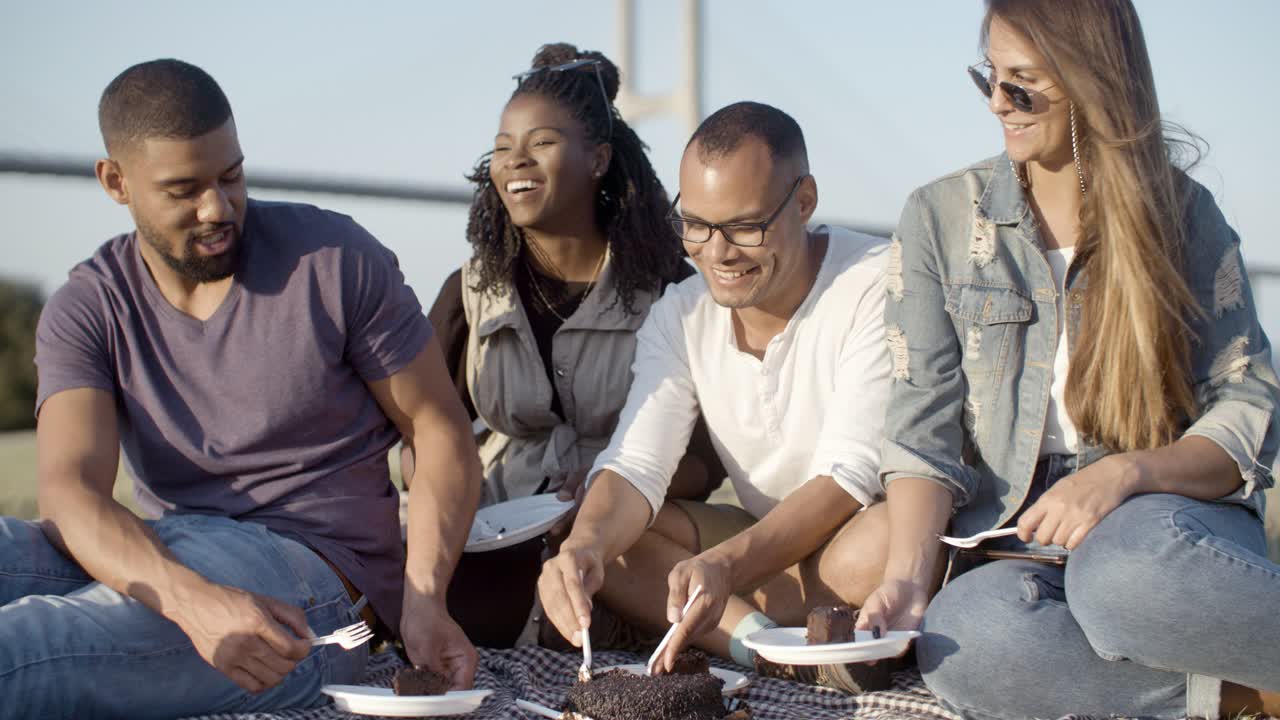 Smiling young man in eyeglasses giving pieces of cake to friends
