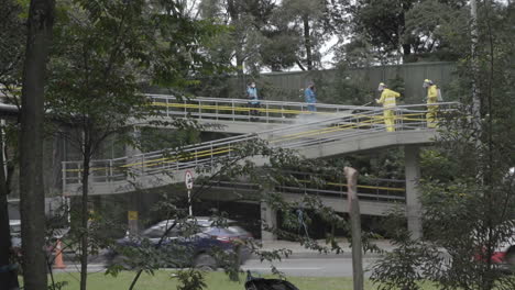 sanitation workers disinfecting an urban overpass with traffic below