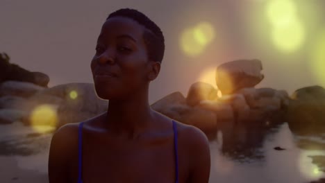 glowing yellow spots of light falling over african american woman walking on the rocks near the sea