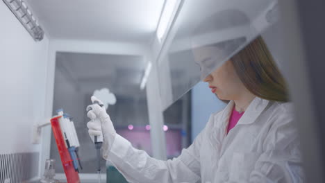 a young female scientist in a lab coat is working in a laboratory, she is holding a pipette and wearing gloves