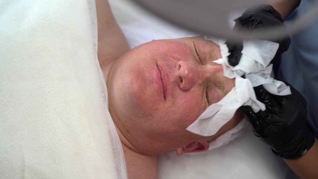 여성 미용사 손은 킨으로 젊은 남자의 얼굴을 청소합니다. 남자는 얼굴의 피부를 돌봅니다.