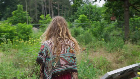 free hippie young person walking back to camera through wild flowers field in nature, organic sustainable agriculture ecovillage tinyhouse lifestyle