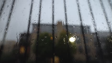 an abstract close up shot of a window covered in rain droplets, as more rain falls the water runs down the window on a dark grey gloomy day during thunderstorm lightning