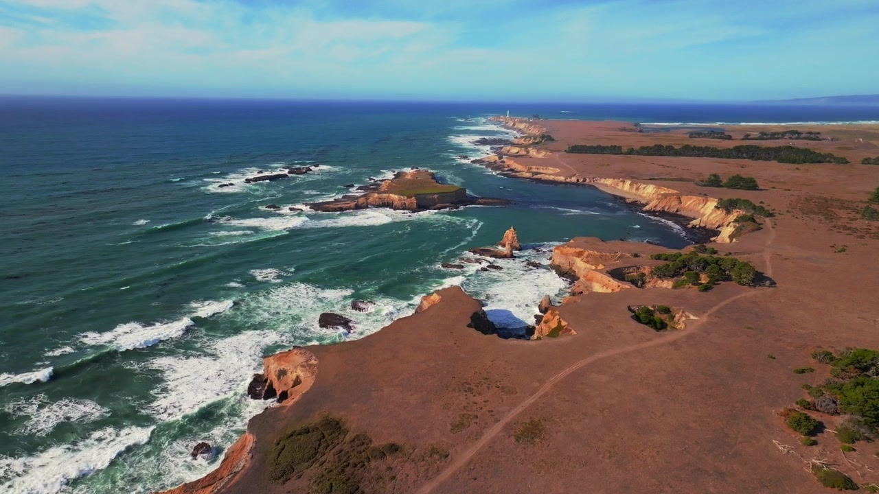 Vista aerea con drone in una giornata di sole della costa di Mendocino, con il Faro di Point Arena Rock, la costa frastagliata della California, le onde che si infrangono sulle rocce. Fort Bragg, San Francisco, Oceano Pacifico settentrionale. Il drone avanza lungo un sentiero escursionistico costiero.