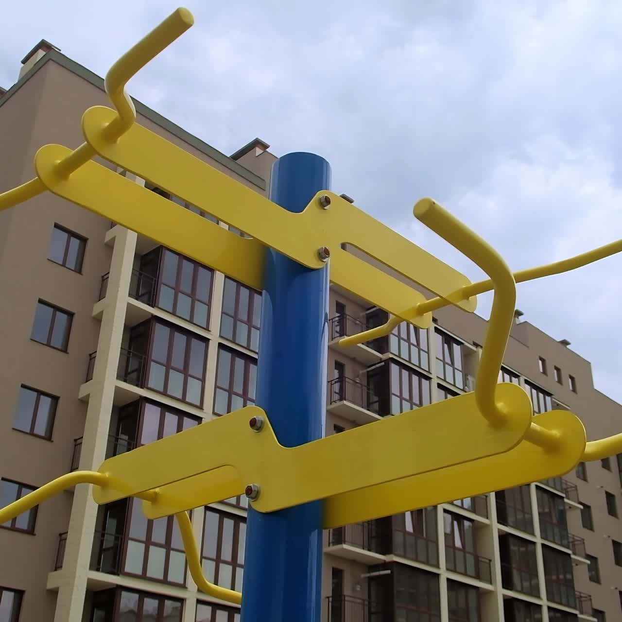 Blue and yellow horizontal bar for workout outdoors. Sports ground near the multi-storied residential building. Low angle view