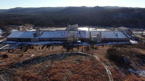 aerial drone footage flying down a hill towards an abandoned brick factory in the middle of winter