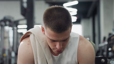 portrait of fitness enthusiast sits on weight bench with towel draped over shoulder exhaling relief after intense chest press workout under modern gym lights showing focused calm expression