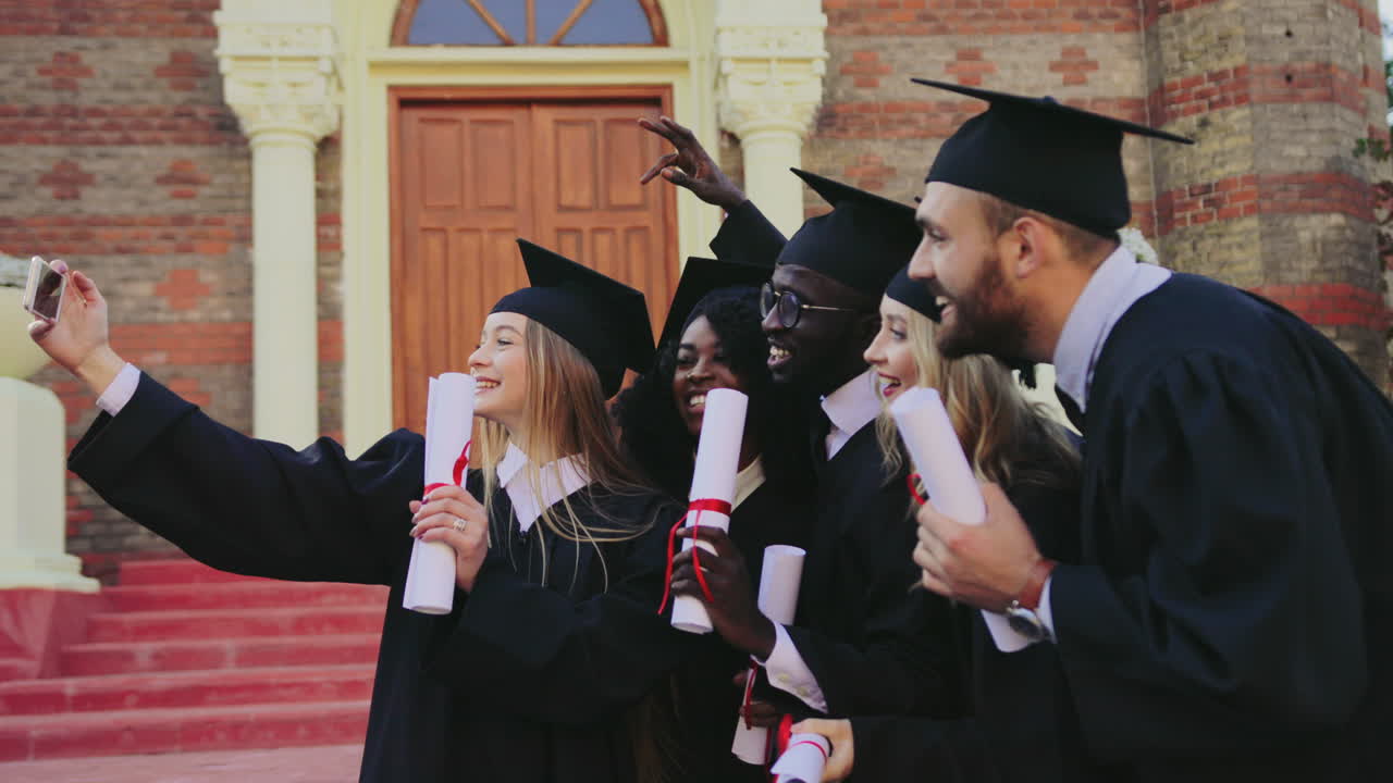 대학 근처에서 졸업장을 들고 스마트폰으로 셀카를 찍는 다민족 졸업생 그룹