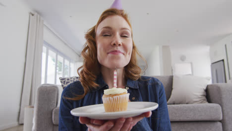 portrait of woman in party hat blowing candle on the cake