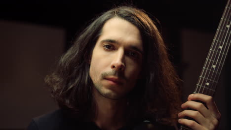 Guitarist-holding-fretboard-in-studio.-Male-musician-looking-to-camera.