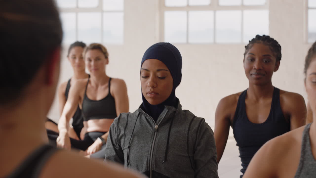gesunde yoga-frau praktiziert lotussitz. junge muslimische frau mit kopftuch genießt den fitness-lebensstil und trainiert im studio mit einer gruppe gemischtrassiger frauen