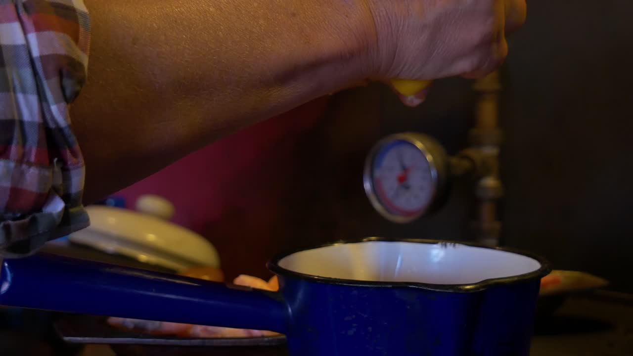 Primo piano a mano libera di una donna anziana che sprema un limone in una pentola per un delizioso piatto Cajun in una cucina di campagna leggermente sporca e vecchia con un idrotermometro sullo sfondo.