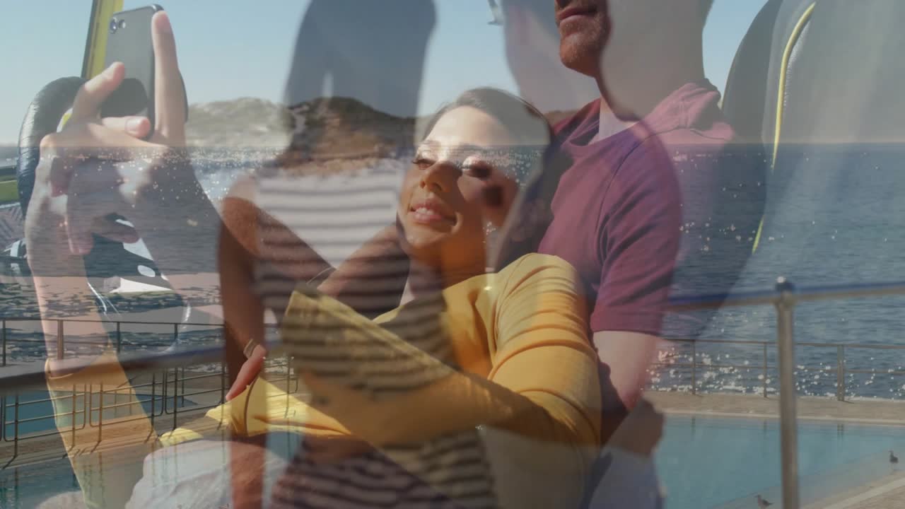 Pareja tomándose una selfie junto al océano, con agua brillante y vista panorámica.