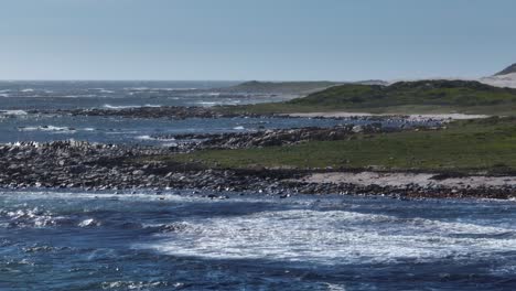 low aerial panning shot of a rocky shoreline with low hills and waves rolling in