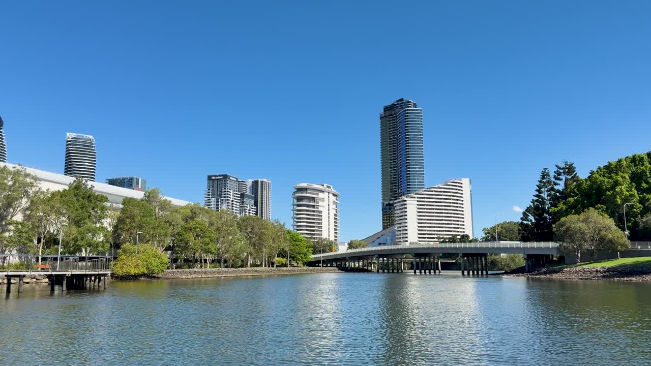 Steady wide shot of modern skyscrapers, river, and greenery in bright daylight, minimal camera movement