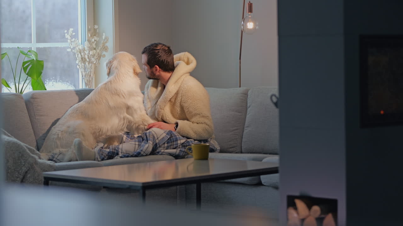 Man relaxing on a cozy sofa with his golden retriever, enjoying a warm, peaceful moment