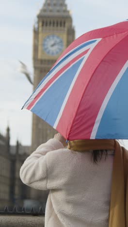 video vertical de una mujer de vacaciones tomando una foto de las casas del parlamento en londres, reino unido bajo el paraguas de union jack