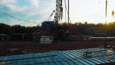 Cinematic-4K-Drone-Footage-of-Onshore-Drilling-Rig-equipment-structure-for-oil-exploration-and-exploitation-in-the-middle-of-jungle-surrounded-by-palm-oil-trees-during-sunset-and-high-oil-price