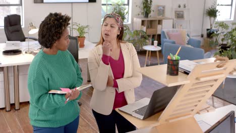 diverse business female colleagues in discussion using laptop in casual office meeting, slow motion