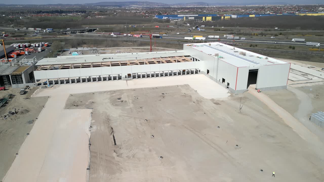 Aerial view of an industrial warehouse under construction with open roof sections and surrounding area