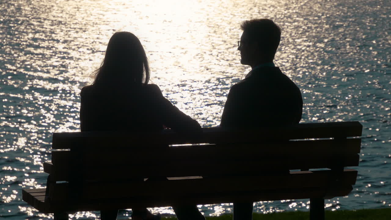 Young coed professional partners meet and talk business while sitting silhouetted by a sunset near a beautiful lake