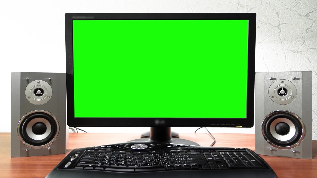 Dataskjerm med grønn skjerm står på et skrivebord på et kontor i timelapse hyperlapse med fremoverbevegelse. Arbeidsplassdesign med lydhøyttalere og svart tastatur.