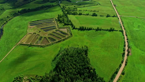 Drones-Aéreos-Vuelan-Lentamente-Sobre-Campos-Agrícolas-Verdes-Con-Estanques-De-Agua,-Senderos-De-Ríos-Que-Cruzan-Un-Bosque-Verde,-Fondo-Del-Horizonte,-Estableciendo-Tomas