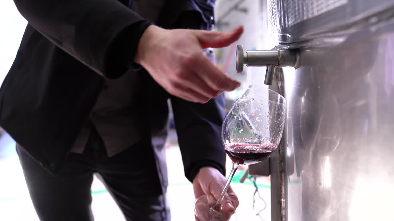 Person pours red wine from stainless steel fermentation tank into a tasting glass
