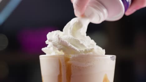 spraying whipped cream over a vanilla milkshake side view close up