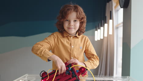 portrait of red-haired boy putting robo boat in water