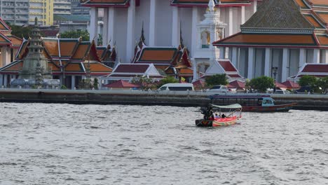 un barco viaja a lo largo de un río con templos a la vista.