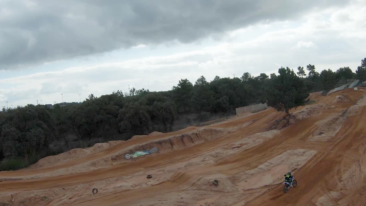 Panoramica aerea che segue un pilota di motocross al rallentatore che salta sbandando la ruota posteriore.