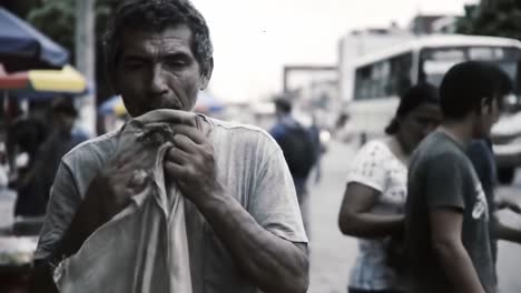 a man dressed in worn clothing walks through bustling streets filled with people and cars during the evening. he appears deep in thought, reflecting on his circumstances amidst the crowd.
