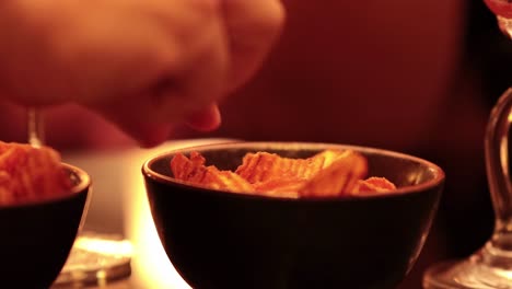 close-up of hands reaching into a bowl of snacks under cozy, ambient lighting.