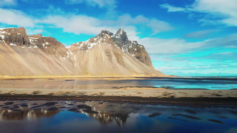 hombre corriendo hacia la montaña vestrahorn en el sur de islandia en un cielo azul nublado - disparo de drones