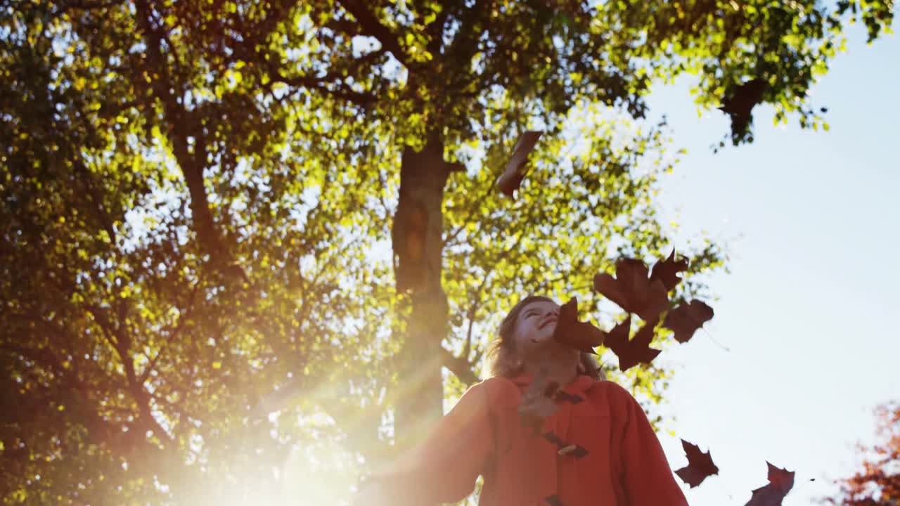 chica arrojando hojas en el parque