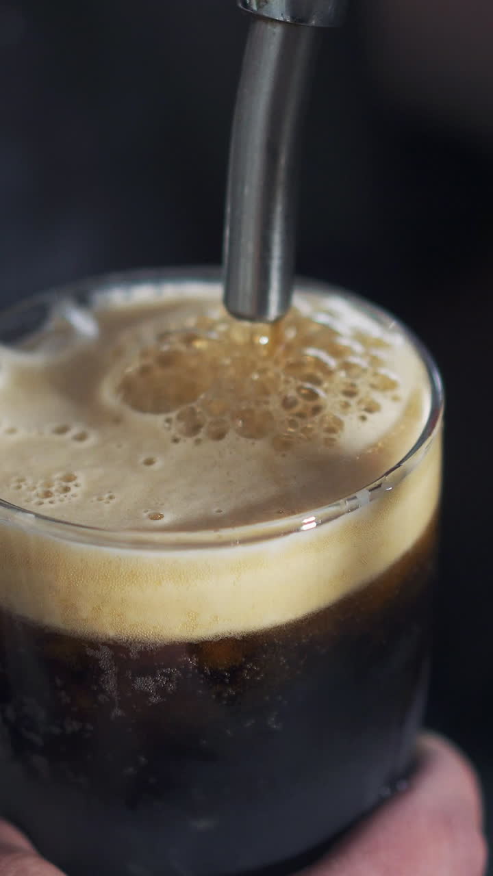Close up of barman's hand pouring beer from the beer tap into the glass in the pub. Process of pouring beer with foam. Vertical video.