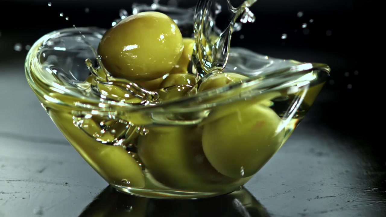 Movimento rallentato di olive verdi che cadono nell'olio d'oliva in una ciotola di vetro