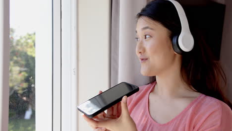 using smartphone and wearing headphones, woman talking and looking out window