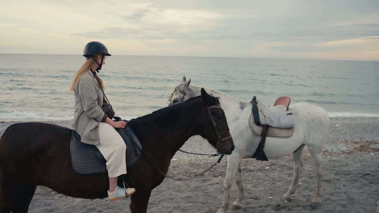 穏やかな午後の海辺で、馬に乗って微笑む若い女性。子供のような熱意と喜びが伝わる映像。