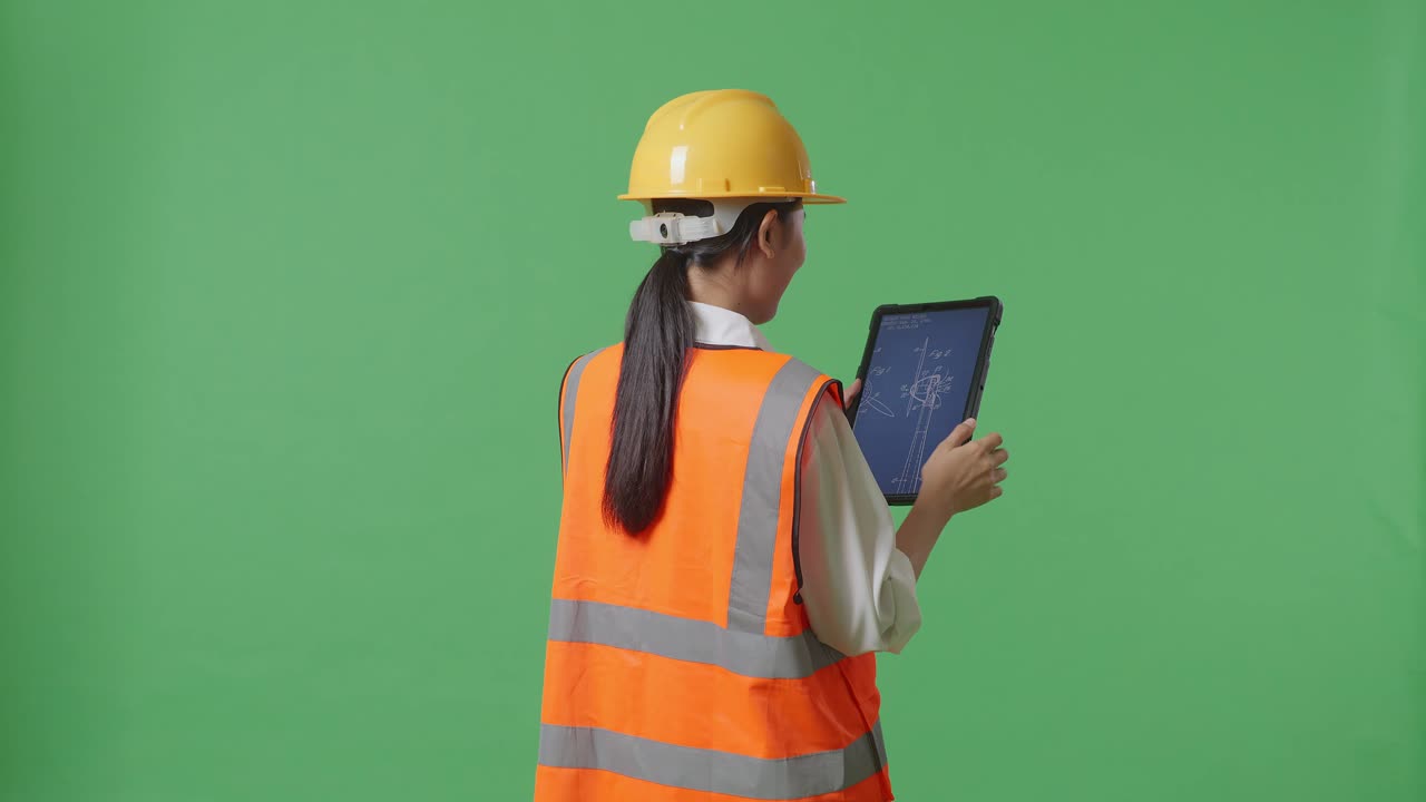 안전 헬을 입은 아시아 여성 엔지니어가 녹색 스크린 배경 스튜디오에 서 있는 태블릿에서 풍력 터빈 블루프린트를 보고 있는 뒷면