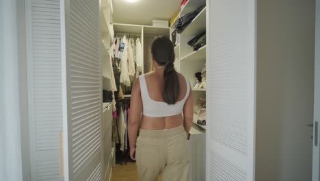 a pregnant woman standing in a modern walk-in closet, thoughtfully selecting an outfit. the scene features stylish clothing and a serene, cozy atmosphere