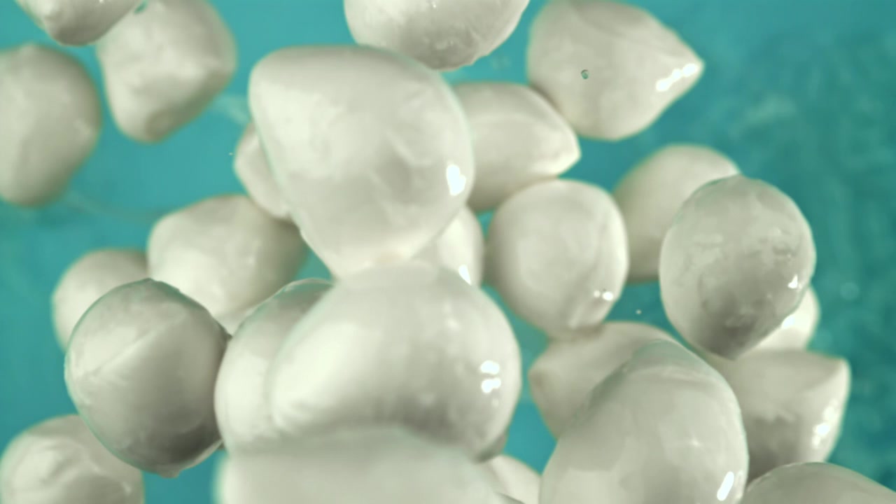 Mini mozzarelle fresche che galleggiano in acqua blu al rallentatore