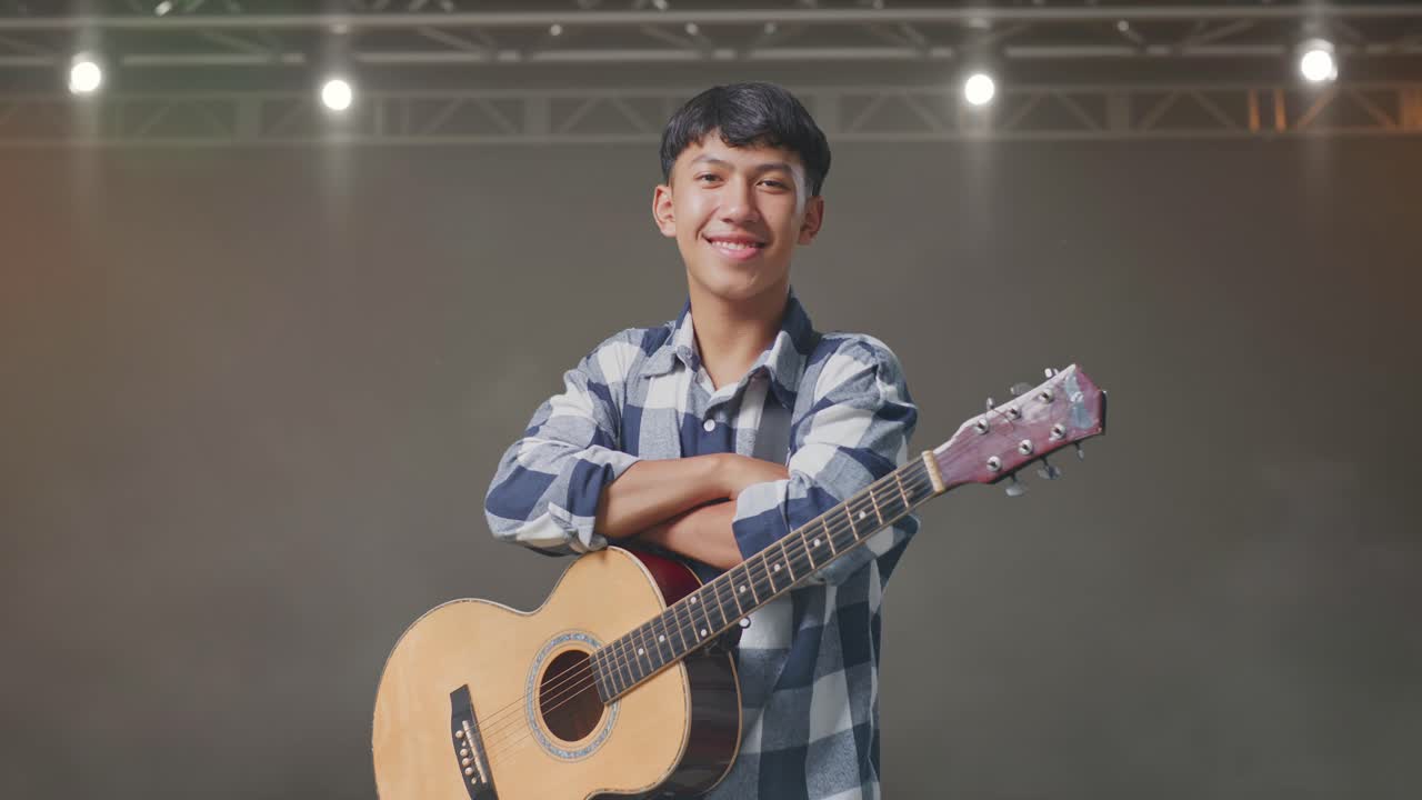 기타를 들고 팔을 고 무대에서 미소 짓는 아시아 십대